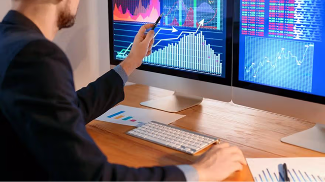 Person analyzing trading charts on multiple screens